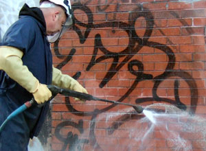 Man removing graffiti from brick wall with hose
